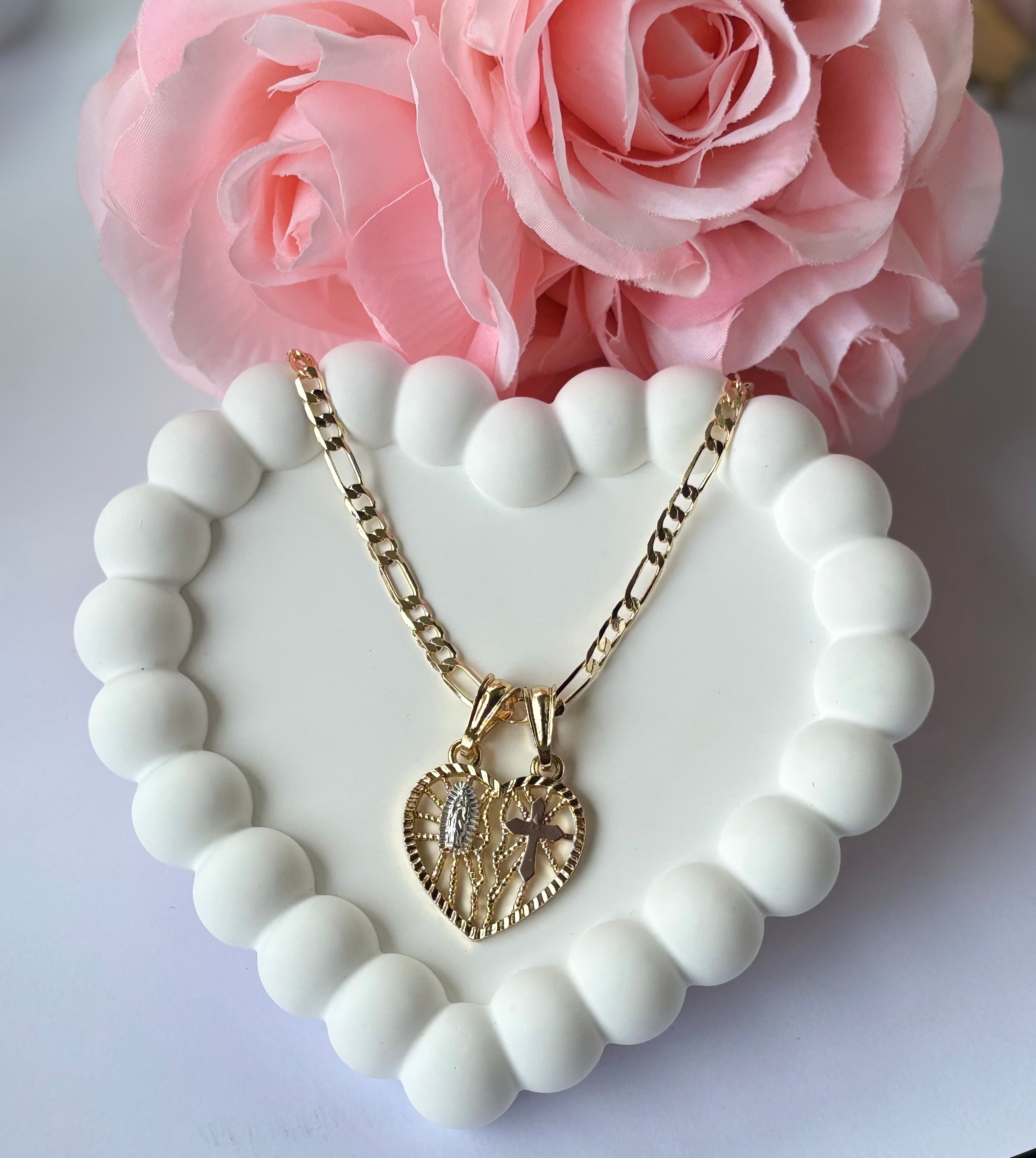 Breakable Heart Necklace in gold plating with Virgencita and cross design, displayed on a white beaded heart tray with pink roses. Comes with two Figaro chains.