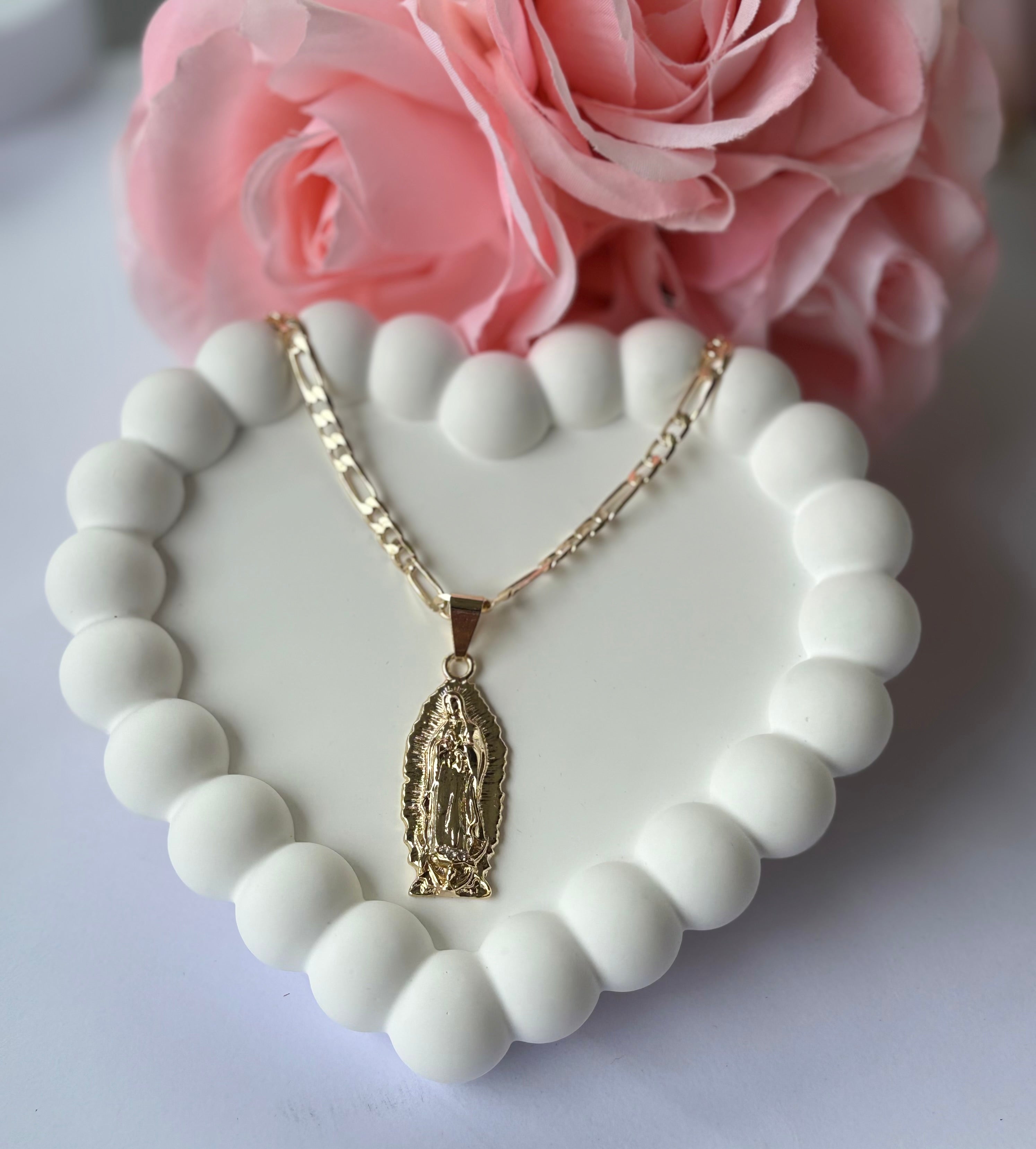 Gold plated Virgen de Guadalupe necklace with Figaro chain, displayed on a white beaded heart tray with pink roses.