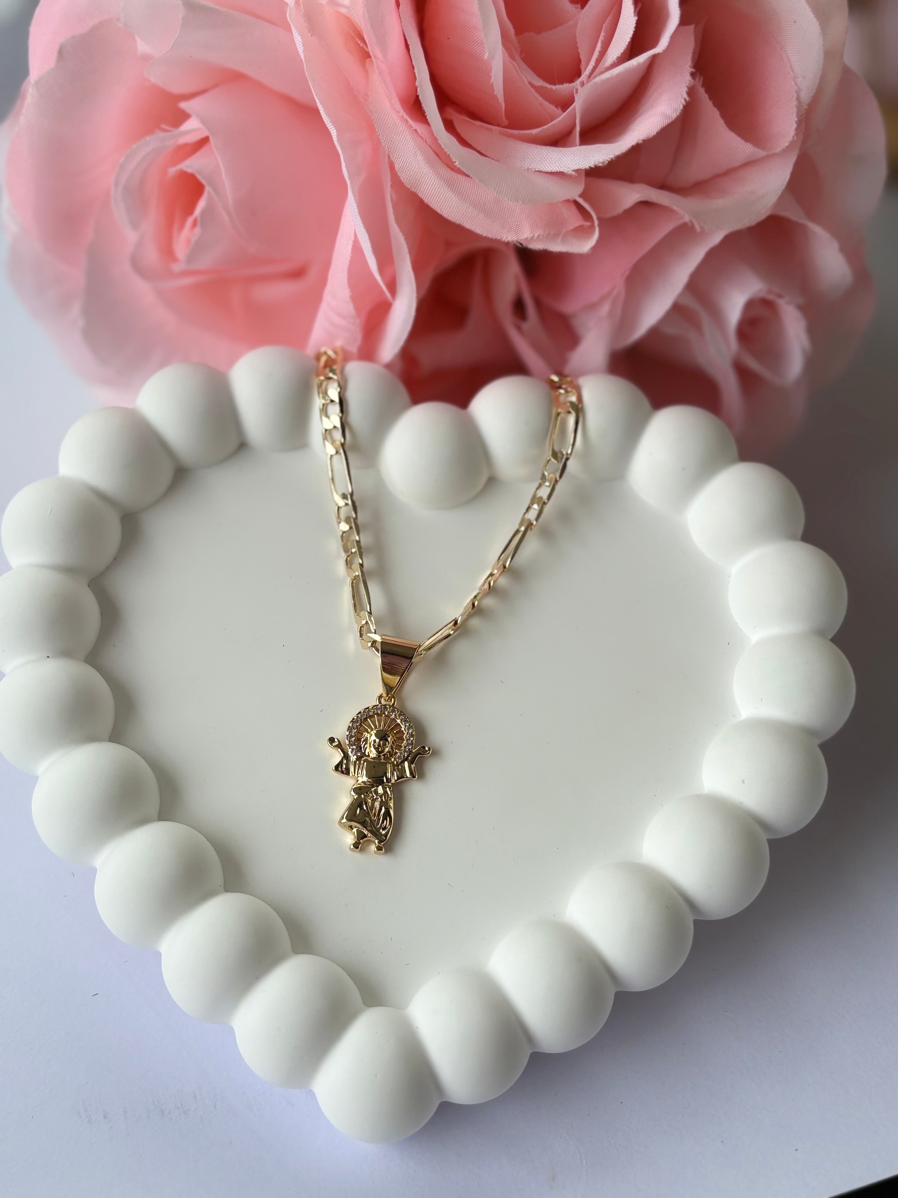 Gold plated Divino Niño Jesús necklace with detailed pendant, displayed on a white beaded heart tray with pink roses.