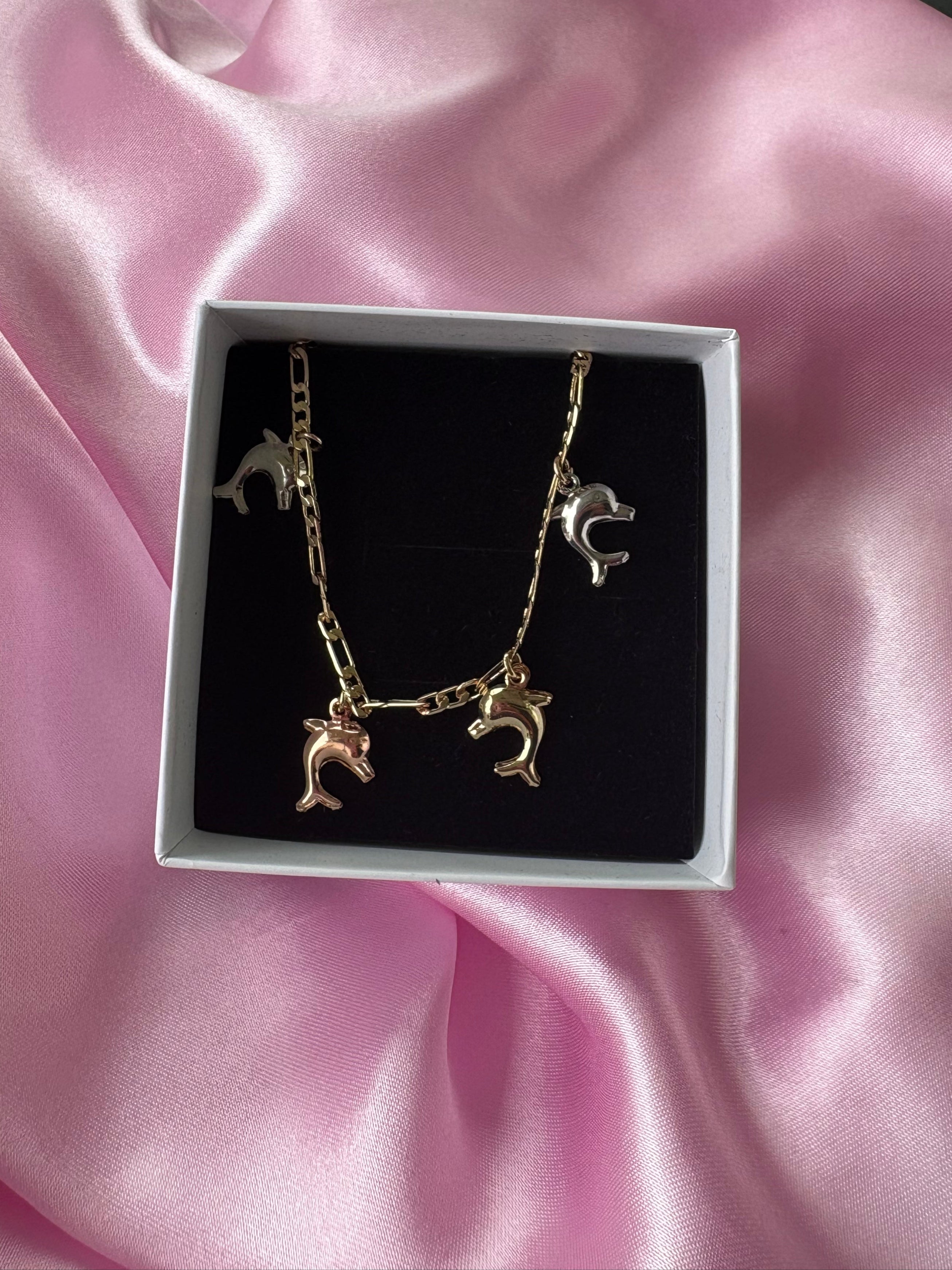 Gold plated charm bracelet with small dolphin pendants, displayed on pink satin background.