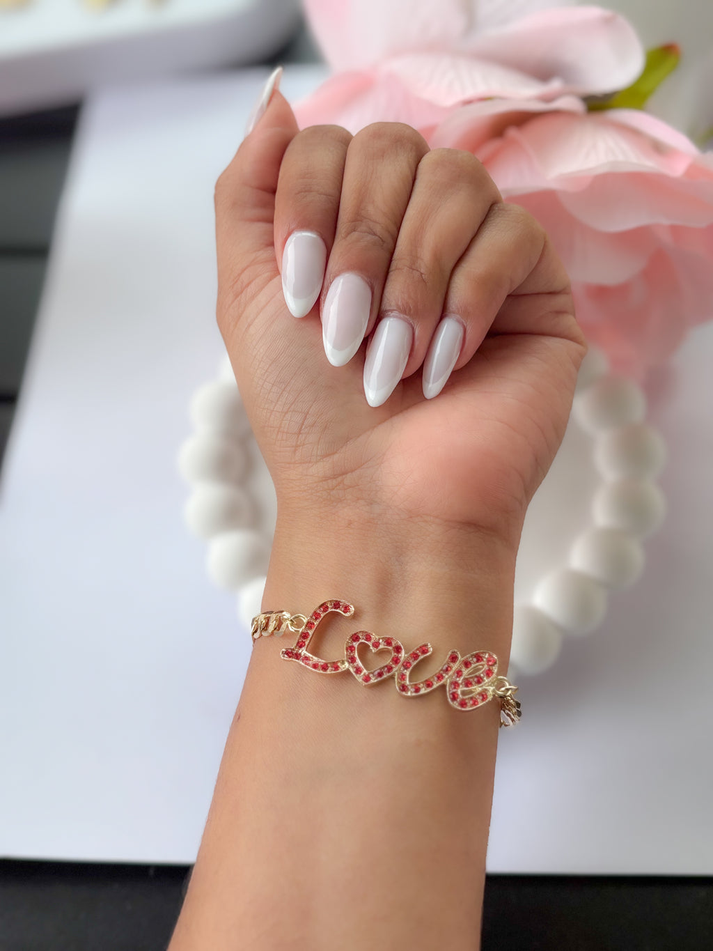Hand wearing a gold bracelet with 'LOVE' on a blurred floral background