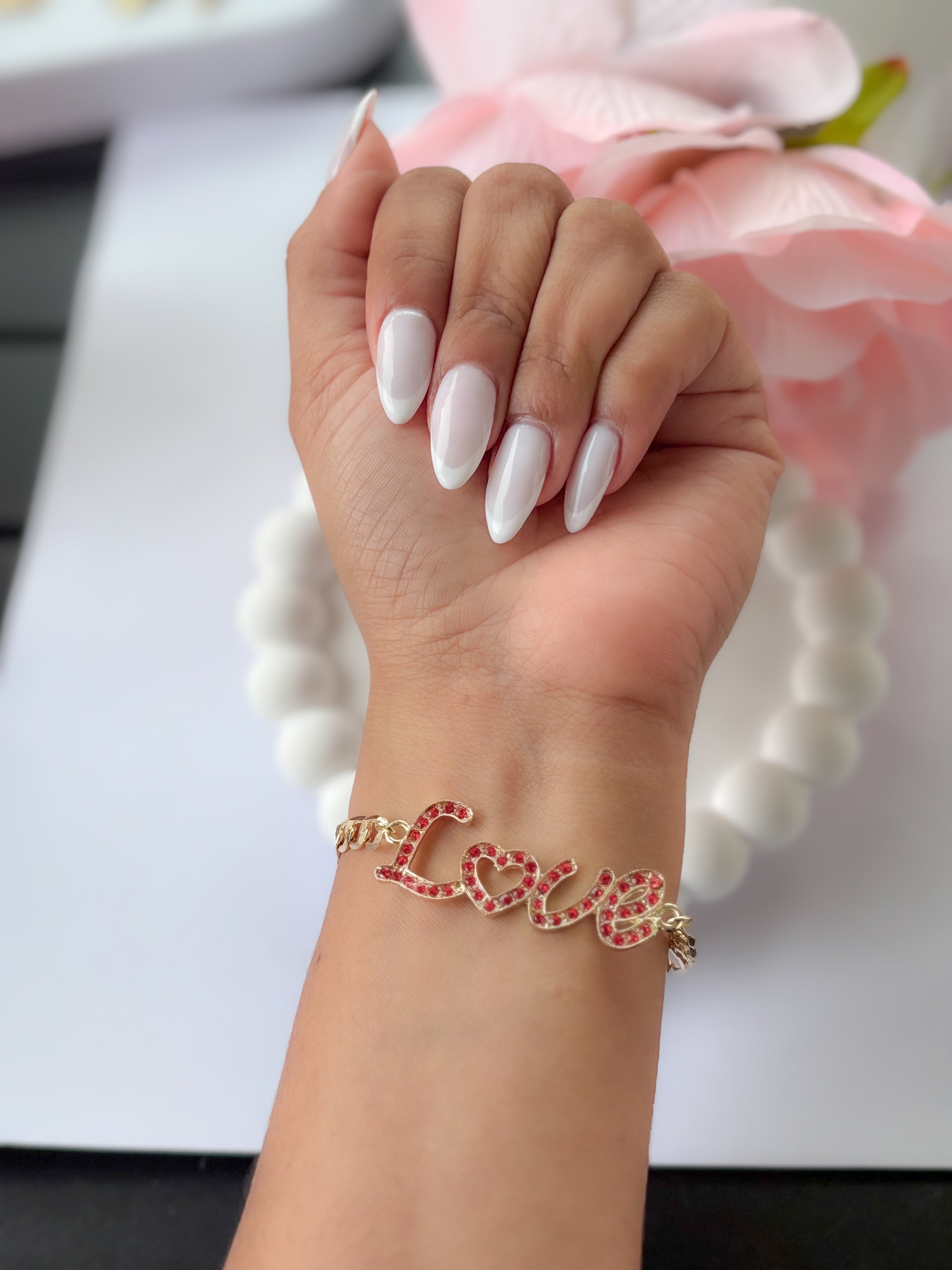Hand wearing a gold bracelet with 'LOVE' on a blurred floral background