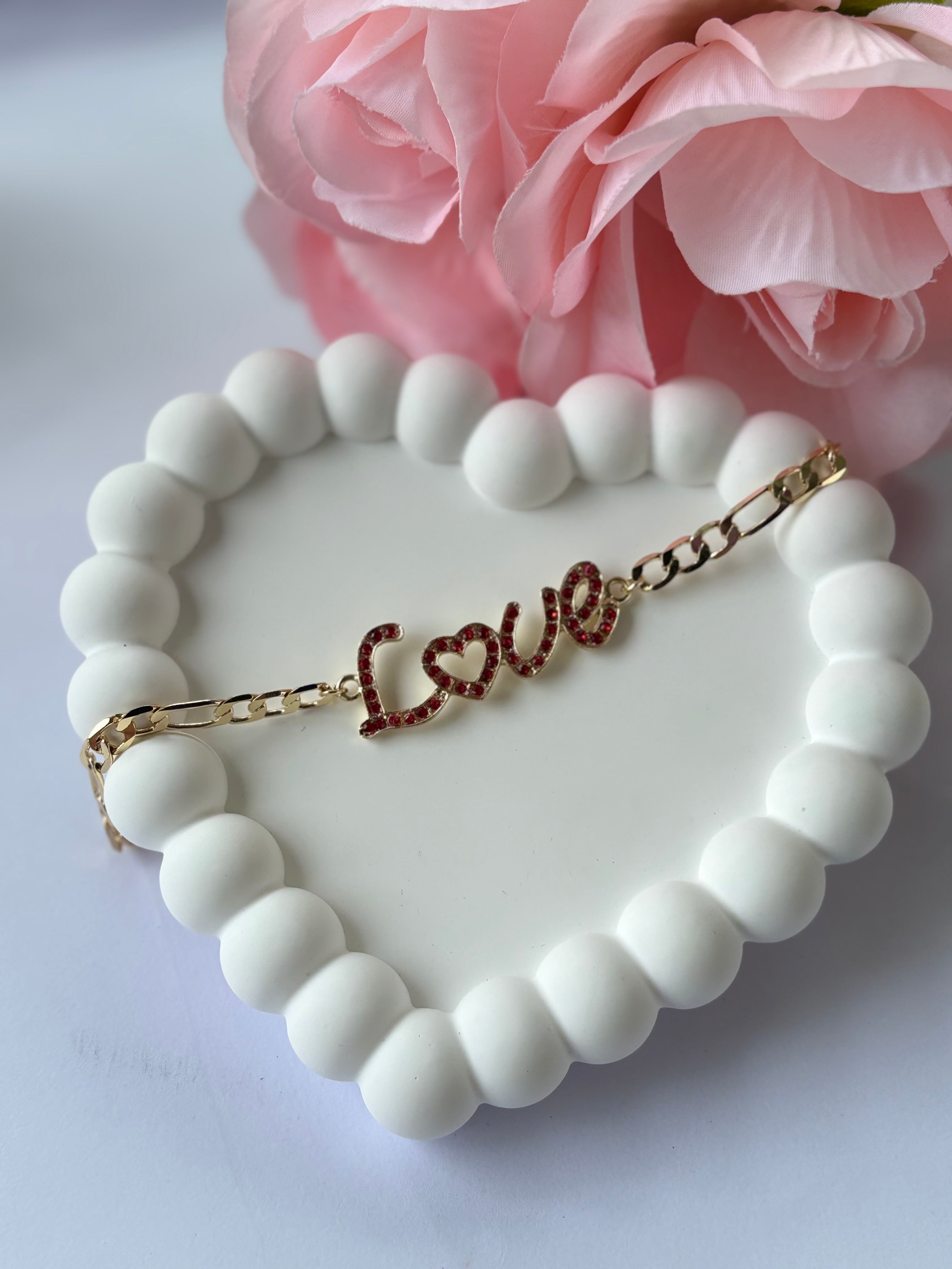 Bracelet with 'LOVE' charm on a heart-shaped white dish with pink flowers in the background