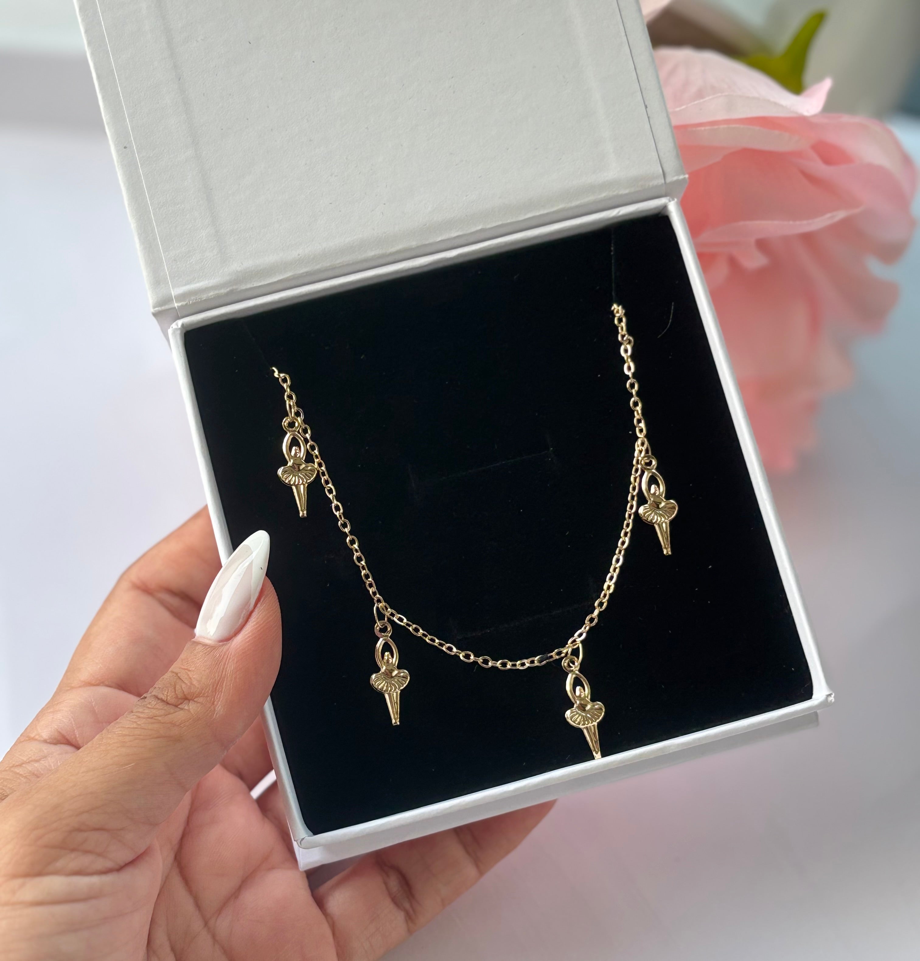 Gold-plated ballerina charm necklace with multiple tiny dancer pendants, displayed in white gift box.